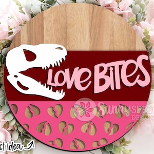 May include: A round wooden sign with a pink and red background. The sign features a white dinosaur skull with the text "Love Bites" in pink letters.