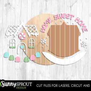 K&ouml;nnte beinhalten: Ein Holzschild mit einem Lebkuchenhaus-Design. Das Schild zeigt die Worte "Home Sweet Home" in Rosa sowie dekorative Elemente wie Schneeflocken, Fenster und S&uuml;&szlig;igkeiten. Entworfen f&uuml;r Laserschneiden und Cricut-Maschinen.