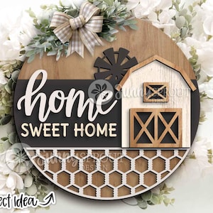 May include: A round wooden farmhouse-style sign with the words "home SWEET HOME" in white script. The sign features a barn, windmill, and a decorative honeycomb pattern. A plaid bow and greenery adorn the top. The words "Project Idea" are at the bottom.