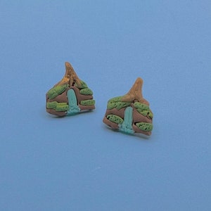 May include: A pair of small, brown and green clay earrings shaped like houses with a blue door and green windows.