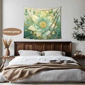 May include: A green and gold floral tapestry with a large, detailed flower in the center. The tapestry is hanging on a white wall above a wooden bed with a white duvet and a brown throw blanket.