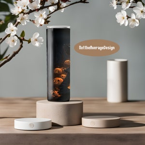 May include: A black and white tumbler with a design of orange pumpkins on a dark background. The tumbler is on a light brown round pedestal. The text "NottheaverageDesign" is visible in the background.