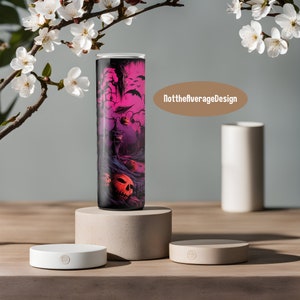 May include: A black and white tumbler with a pink and purple Halloween themed design. The design features a spooky house, bats, and pumpkins. The tumbler is sitting on a beige platform. The text "NottheaverageDesign" is visible in the image.