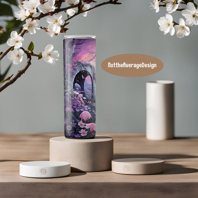 May include: A white ceramic coaster with a small black logo. The coaster is sitting on a wooden surface. A tall, cylindrical tumbler with a colorful floral design is sitting on a larger, beige ceramic coaster. The tumbler has a pink, purple, and blue floral design with a dark blue background. The text "NottheaverageDesign" is visible in the background.