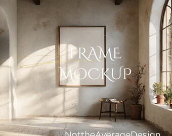 May include: A rustic interior design mockup featuring a large, empty picture frame with a gold frame hanging on a white wall. The frame is centered in the image and is surrounded by natural light. The text "FRAME MOCKUP" is visible in the image.