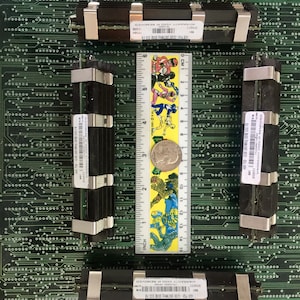 May include: Two black computer memory modules with silver clips are installed on a green circuit board. The modules have labels that read "1GB PC2-5000 (667MHz) DDR2 ECC FB" and "WARRANTY VOID IF REMOVED". A ruler is placed between the modules.