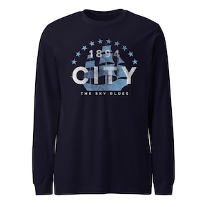 May include: Navy blue long-sleeve shirt with a light blue graphic. The graphic features a ship, the word "CITY", the year "1894", and the text "THE SKY BLUES" surrounded by stars. The shirt is made of a soft material.