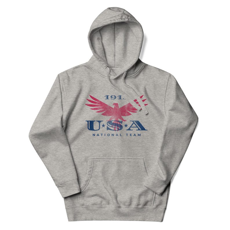 Może przedstawiać: Szara bluza z kapturem z przednią kieszenią i sznurkiem. Z przodu znajduje się czerwono-niebieska grafika orła z napisem "1911 USA NATIONAL TEAM".