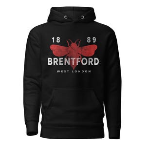 Könnte beinhalten: Schwarzer Kapuzenpullover mit roter und weißer Grafik. Die Grafik zeigt eine stilisierte Biene mit dem Text "BRENTFORD WEST LONDON" und den Zahlen "18 89". Der Kapuzenpullover hat eine Vordertasche und eine Kapuze mit Kordelzug.