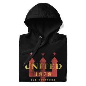 May include: Black hooded sweatshirt with a graphic design. The design features the word "UNITED" in yellow, the number "1878", and the words "OLD TRAFFORD" in white. Above the word "UNITED" are three red stars.