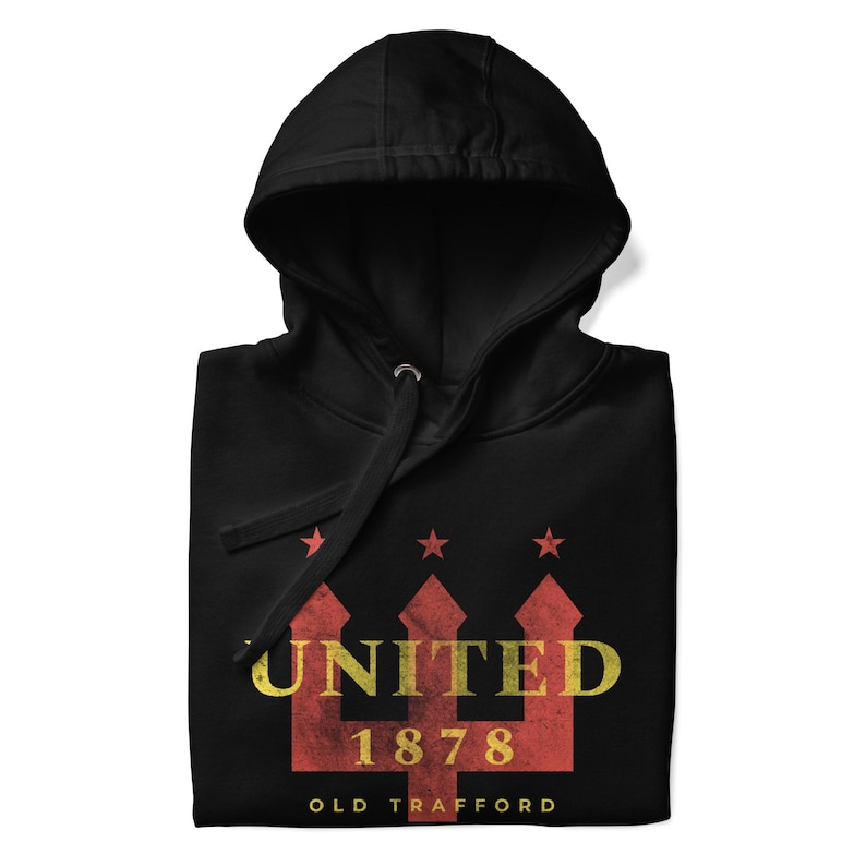 May include: Black hooded sweatshirt with a graphic design. The design features the word "UNITED" in yellow, the number "1878", and the words "OLD TRAFFORD" in white. Above the word "UNITED" are three red stars.