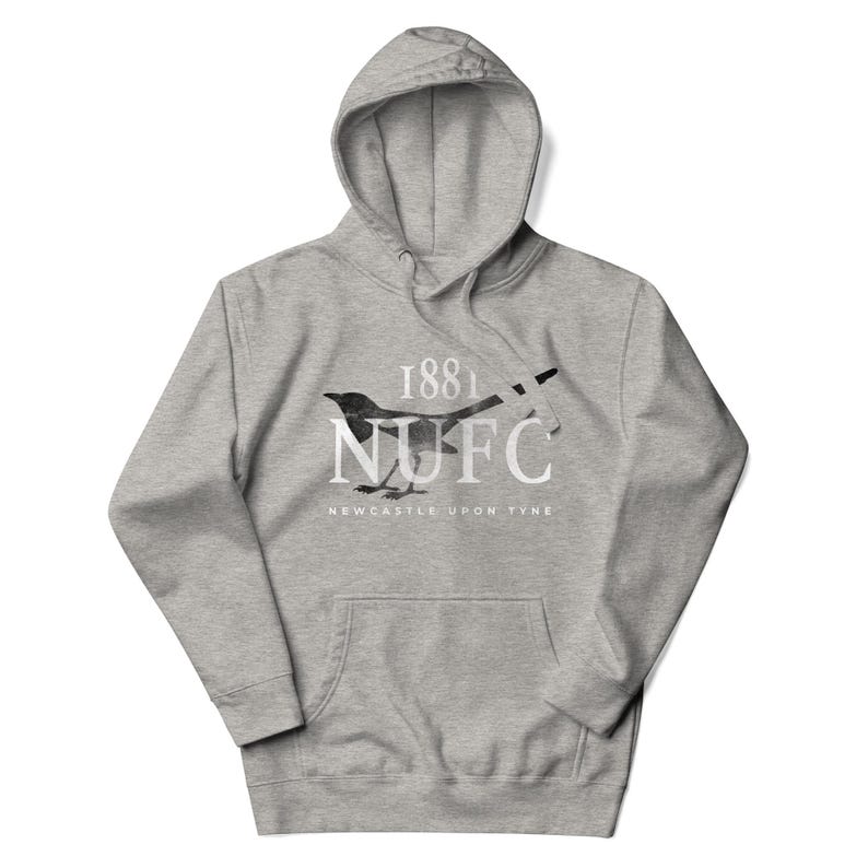 May include: A gray hooded sweatshirt with a front pocket. The sweatshirt features a black and white magpie design with the text "1881 NUFC NEWCASTLE UPON TYNE". The hoodie is made of a soft material.