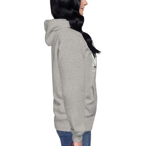 May include: A heather gray hoodie with a front pocket and a drawstring hood. The hoodie features the white text "N" and "NEW" printed on the front. The model is wearing blue jeans.