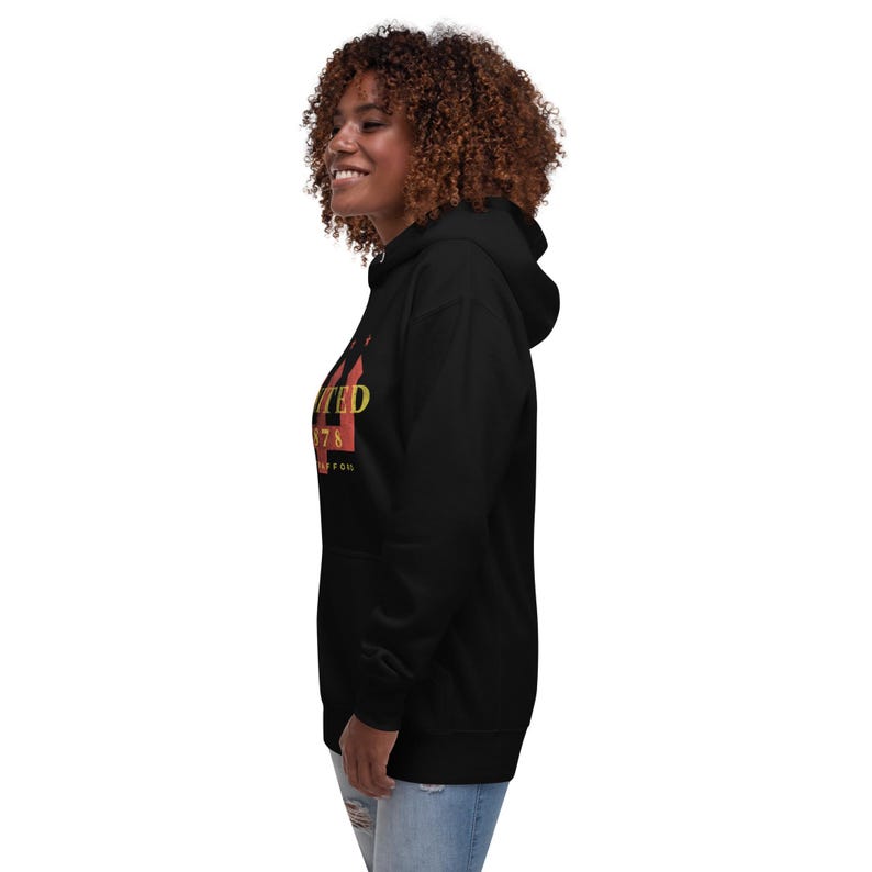 May include: Black hooded sweatshirt with the word "UNITED" in yellow and red block letters. The number "78" is below the word "UNITED". The sweatshirt is worn by a person with curly brown hair.