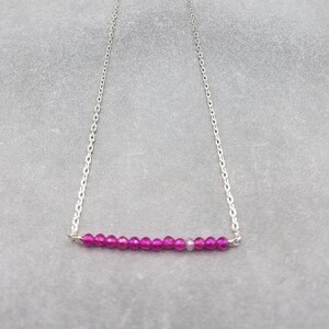 May include: A silver chain necklace with a bar of pink beads.