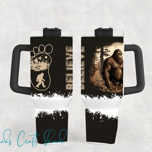 May include: A black and white stainless steel tumbler with a black handle. The tumbler has a design of a Bigfoot footprint with the words "Believe" and "Bigfoot" on the side. The other side of the tumbler has a design of a Bigfoot standing in a forest.