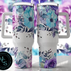 May include: A white stainless steel tumbler with a floral design featuring blue, purple, and gray watercolor flowers. The tumbler has a white handle and a white lid. The tumbler is 20 ounces.