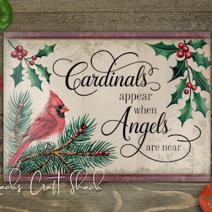 May include: A decorative cutting board with a red cardinal perched on a branch of pine needles. The background features holly leaves and berries. The text reads "Cardinals appear when Angels are near".