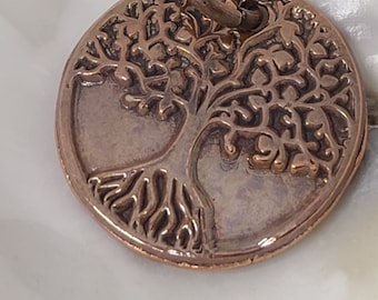 May include: A copper-colored pendant featuring a detailed tree of life design. The pendant has a loop at the top for attaching to a chain or cord.