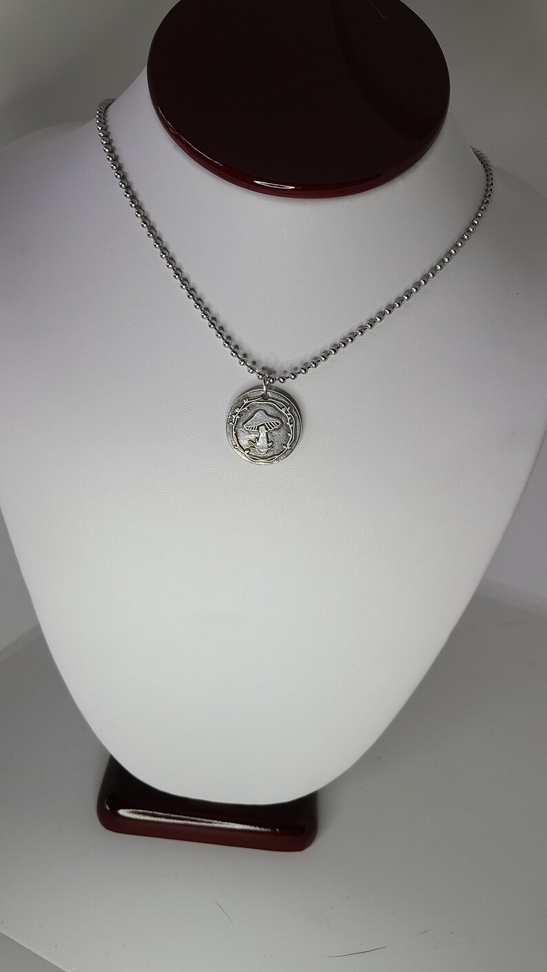May include: A silver chain necklace with a round pendant featuring a detailed mushroom design.