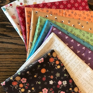 May include: A stack of 12 fabric squares with various floral patterns and colors, including white, red, orange, green, blue, purple, and brown. The fabric squares are arranged in a fan shape, with the top square being white with small floral patterns and the bottom square being brown with larger floral patterns.