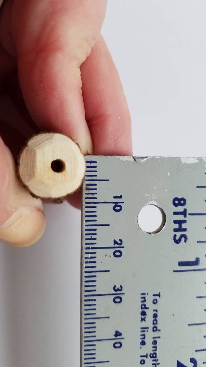 May include: A close-up of a wooden dowel with a hole drilled through the center. The dowel is being measured with a ruler, showing it is approximately 1 inch in length.