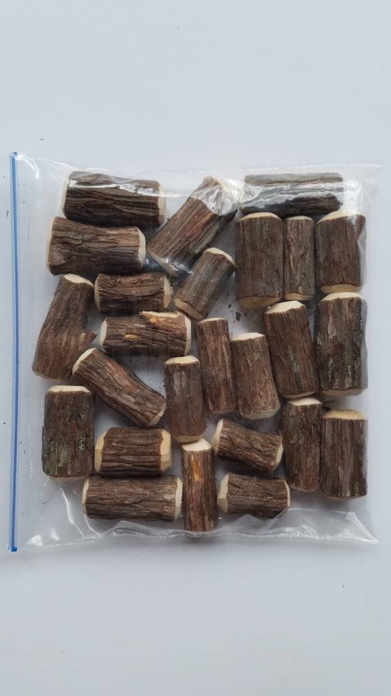 May include: A clear plastic bag filled with small, brown wooden logs. The logs are approximately 1-2 inches in length and have a natural, rustic appearance.