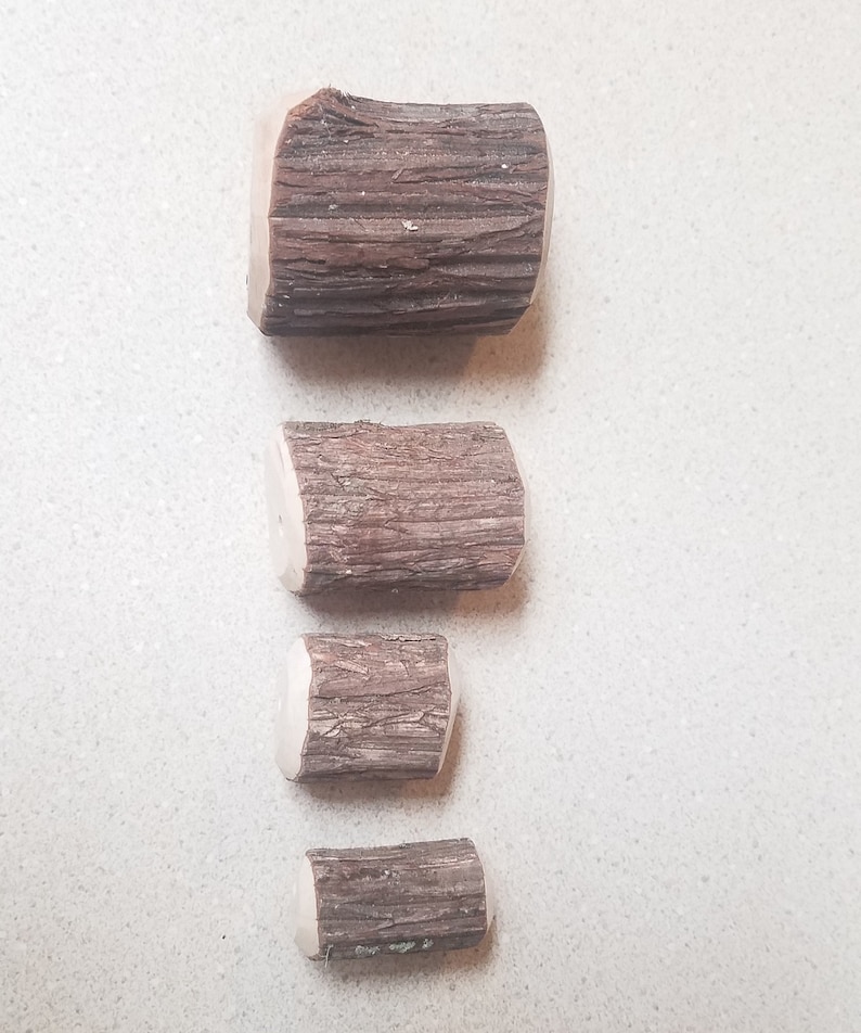 May include: Four wooden log slices of varying sizes, arranged vertically from largest to smallest. The logs are brown with a natural bark texture.