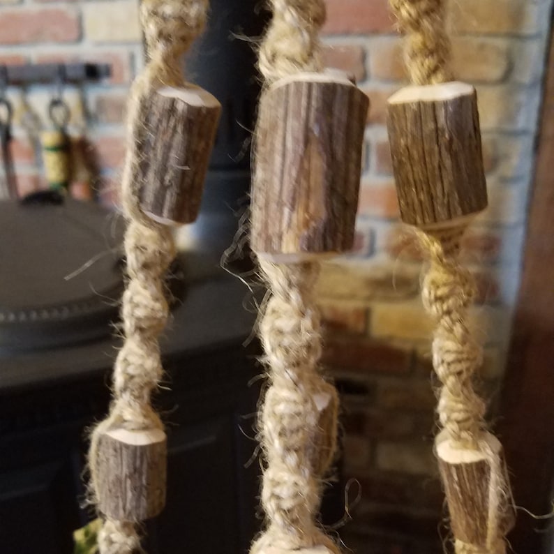 May include: A close-up of a macrame wall hanging with wooden beads. The beads are made of natural wood and have a rustic look. The macrame is made of natural fiber rope and has a knot pattern.