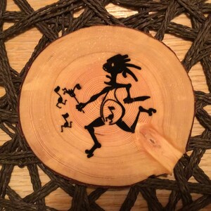 Puede incluir: Un disco redondo de madera con una silueta negra de una persona bailando con notas musicales. El disco está sobre una superficie de tejido marrón.