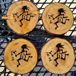 Puede incluir: Cuatro posavasos redondos de madera con vetas naturales. Cada posavasos presenta una silueta negra de una figura corriendo con un diseño único. Los posavasos están dispuestos sobre una superficie metálica negra.