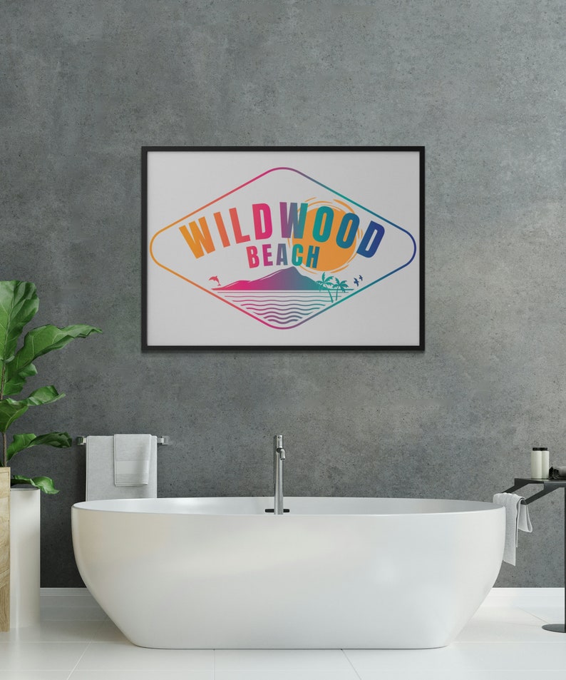 May include: A framed print featuring a colourful graphic design of a diamond shape with the text "WILDWOOD BEACH" inside. The graphic depicts a sunset, palm trees, and a wave. The print is hanging on a grey concrete wall above a white bathtub.