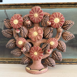 Pu&ograve; includere: Una scultura in terracotta a forma di albero della vita con fiori dipinti a mano dai petali rossi e centri gialli, intervallati da foglie con venature marroni e piccoli boccioli rotondi, il tutto su una solida base circolare opaca.