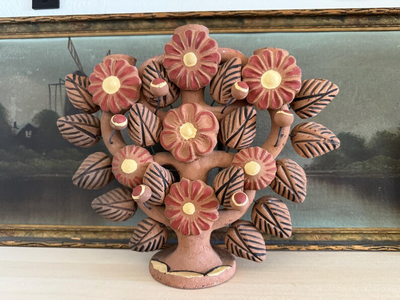 Pu&ograve; includere: Una scultura in terracotta a forma di albero della vita con fiori dipinti a mano dai petali rossi e centri gialli, intervallati da foglie con venature marroni e piccoli boccioli rotondi, il tutto su una solida base circolare opaca.
