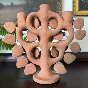Pu&ograve; includere: Un candelabro in terracotta caratterizzato da un tronco centrale e bracci ramificati che formano una struttura ad albero. L'oggetto &egrave; decorato con numerosi dischi di argilla piatti e circolari fissati a sottili fili metallici.