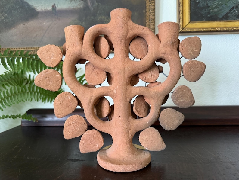 Pu&ograve; includere: Un candelabro in terracotta caratterizzato da un tronco centrale e bracci ramificati che formano una struttura ad albero. L'oggetto &egrave; decorato con numerosi dischi di argilla piatti e circolari fissati a sottili fili metallici.