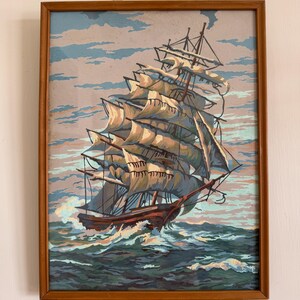 May include: A framed painting of a large sailing ship with white sails against a blue and gray sky. The ship is sailing on a blue and green ocean with white waves.