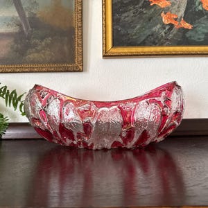 May include: A decorative, curved glass bowl with a textured, clear design and a vibrant red hue. The bowl's shape is reminiscent of a crescent moon, adding a touch of elegance. This piece is ideal for displaying small items or as a standalone decorative accent.