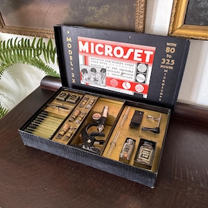 May include: Vintage Microset Model 3X microscope kit in a black box. The box contains a microscope, slides, and various scientific tools. The box reads "Discover new worlds under your eyes" and "80 to 325 power microscope".