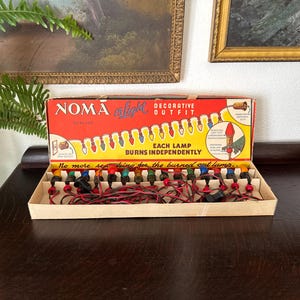 May include: Vintage NOMA 15 Light Decorative Outfit Christmas light set in its original box. The box is red and yellow with text and illustrations. The lights are multi-colored.