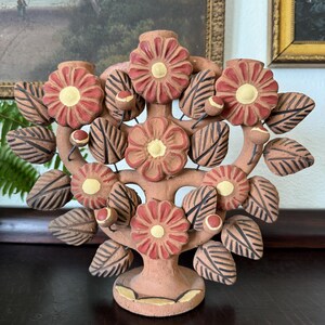 Pu&ograve; includere: Un candelabro in terracotta a forma di albero con cinque portacandele. L'oggetto presenta fiori rossi scolpiti con centri gialli e foglie a strisce marrone scuro. La base &egrave; circolare con accenti gialli e sono presenti piccoli boccioli.