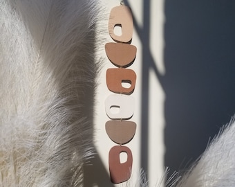 May include: A wall hanging made of five terracotta-colored ceramic shapes, each with a different organic form. The shapes are connected by gold-colored metal rings and hang in a vertical line.