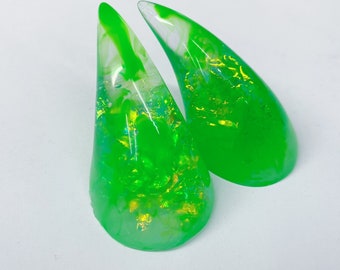 May include: Two green resin horns with gold glitter embedded in the resin. The horns are pointed and have a white swirl pattern.
