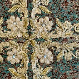 May include: Close-up of a teal fabric with gold embroidery of floral designs. The fabric has a repeating pattern of small flowers and leaves.