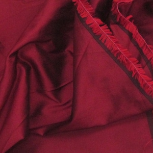 Puede incluir: Tela de color rojo burdeos con ribete de flecos negros y rojos. La tela es lisa y sedosa.