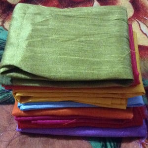 Puede incluir: Un conjunto de muestras de tela en varios colores, incluyendo verde, amarillo, azul, naranja, rosa y morado. La tela está doblada cuidadosamente y parece ser suave y lisa.
