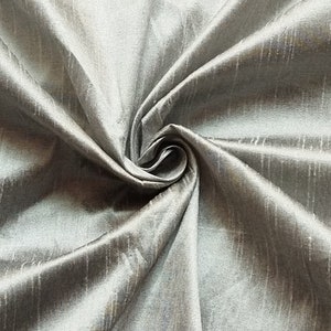 Peut inclure: Un gros plan sur un tissu de soie argenté avec un léger brillant et un motif tissé texturé. Le tissu est drapé et plié, mettant en valeur sa texture douce et luxueuse.