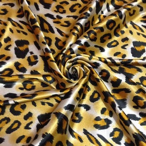 Puede incluir: Primer plano de una tela con estampado de leopardo. La tela tiene un fondo amarillo dorado con manchas negras y marrones. La tela está doblada y arremolinada, creando un efecto texturizado.