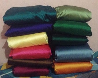 May include: A stack of 10 different colored satin fabrics. The colors are teal, purple, yellow, pink, brown, maroon, green, blue, orange, and olive.
