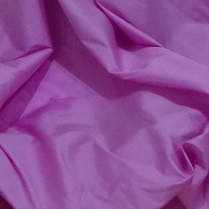 May include: A close-up of a smooth, silky fabric in a vibrant purple hue. The fabric is draped and folded, creating soft, flowing lines.